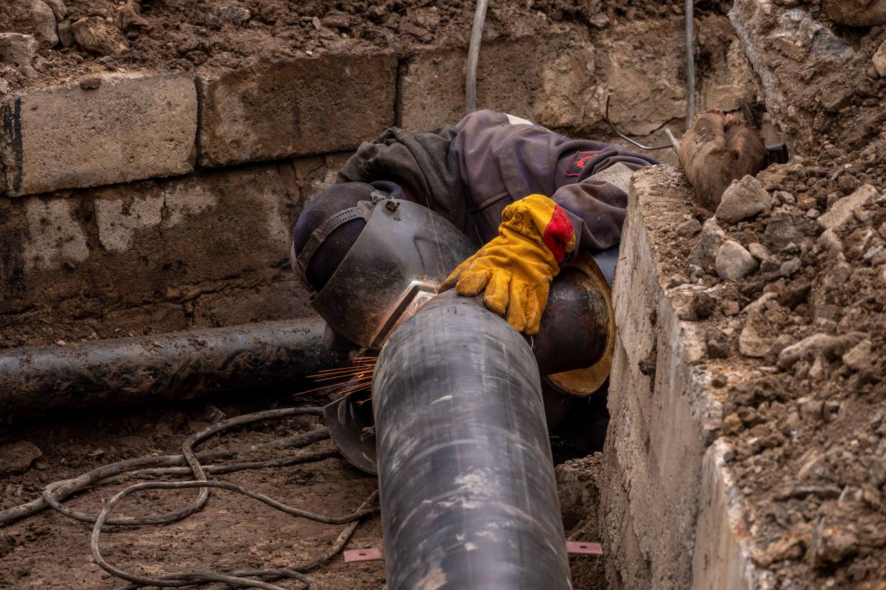 Services A worker welds a pipe in an urban trench, showcasing industrial construction work.